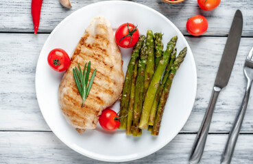 Grilled chicken breast with asparagus and spices on a plate on a wood background 