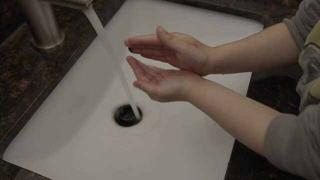 High quality close-up 4k slow motion video of a small boy washing his hands in a granite beautiful sink with soap and running water due to covid 19 and new normal. Baby properly washing his hands