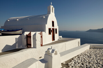 White orthodox church with a traditional boat beside over Santorini caldera