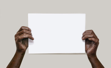 Black male hands hold a blank sheet of white paper on an isolated gray background. The concept of...