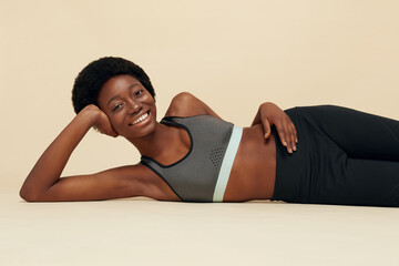 Fototapeta na wymiar Fitness Girl. Portrait Of African Woman. Smiling Female In Sportswear Lying Leaning On Hand. Beautiful Model Relaxing On Floor After Exercising. Sport For Active Lifestyle.