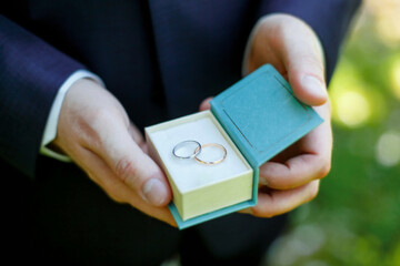 groom is holding a small turquoise box with a couple of wedding rings