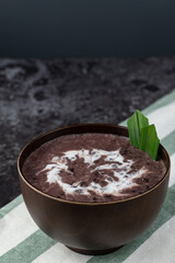 Black Glutinous Rice Porridge or Bubur Pulut Hitam in Malay with coconut milk on dark background on top napkin