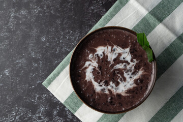 Black Glutinous Rice Porridge or Bubur Pulut Hitam in Malay with coconut milk on dark background on top napkin