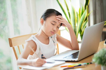 Homeschool Worried and sad little girl using laptop to learn and doing homework on line at home...