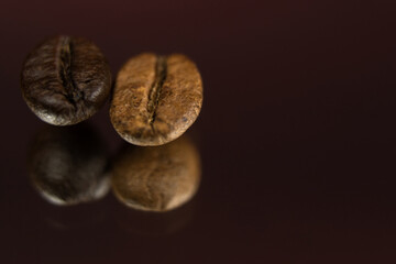 Two roasted coffee beans in a row, horizontal. Extreme close up, macro photography, selective focus. Background deep red, foreground textured black with light effects. Space for copy or text.