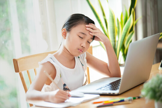 Homeschool Worried and sad little girl using laptop to learn and doing homework on line at home sitting at the table