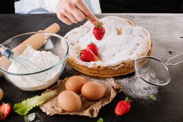 Woman's hand putting strawberry in strawberry pie. Bakery concept.