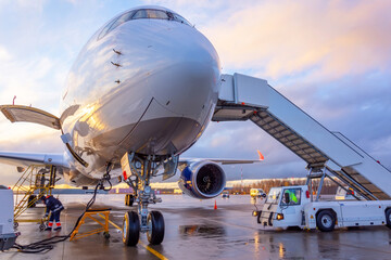 Nose view of an airplane with gangway for boarding parked at an airport during sunset bright light shine and clouds in the sky.