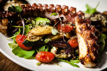Warm octopus salad with stir fried vegetables and aji sauce on white plate. Delicious healthy mediterranean traditional seafood closeup served on a table for lunch.