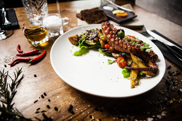 Warm octopus salad with stir fried vegetables and aji sauce on white plate. Delicious healthy mediterranean traditional seafood closeup served on a table for lunch.