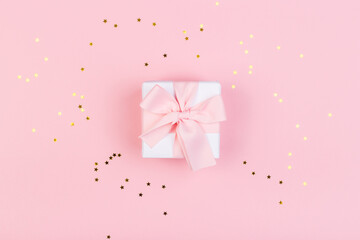 Gift or gift box and stars confetti on a pink table from above. Flat composition for birthday