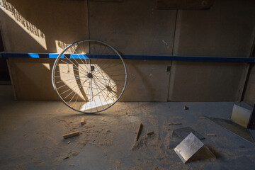 Old bicycle wheel on display in a former bike repair workshop abandoned with other cycle spare parts scattered on the floor.