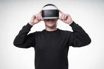 Young man in VR goggles watches a pleasant video and smiles widely, trying to adjust his glasses with hands, white background, studio