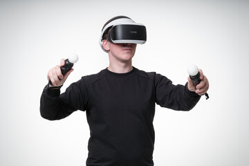 Young man is experiencing VR games with motion sticks and 3D glasses, he is gesticulating wildly and eagerly, white background studio