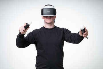 Young man is experiencing VR games with motion sticks and 3D glasses, he is gesticulating wildly and eagerly, white background studio