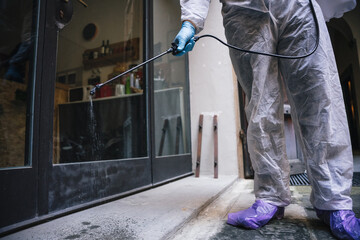 Person specialized in disinfestation and sanitization of work environments spray the liquid on the floor against Coronavirus, Covid-19 - Man with latex gloves and overalls, disinfects surfaces