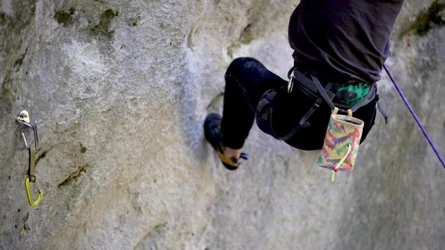 Young rock climber holding grip in rock socket and clipping to quickdraw 
