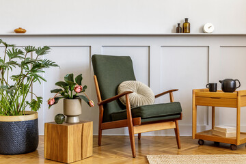 Interior design of stylish living room with vintage green armchair, wooden coffee table, furniture, grey wall, shelf, carpet, plants, clock, book, copy space and elegant personal accessories.