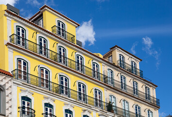 Fototapeta na wymiar Traditional apartment building in Lisbon Portugal - exterior. Bright yellow and white facade with tall windows and long balconies. Portuguese style vintage house with multiple condos.
