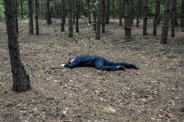 Murder in the woods. The body of a man in a blue shirt and trousers lies on the ground among the trees in the forest. Victim of an attack.