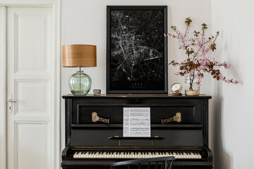 Fototapeta na wymiar Stylish composition at living room interior with black piano, mock up poster map, dried flowers, clock, book, lamp, white wall and elegant presonal accessories in modern home decor.