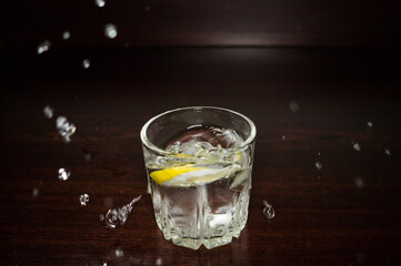 Fototapeta na wymiar Lemon falls into a glass with transparent water and water splashes fly.