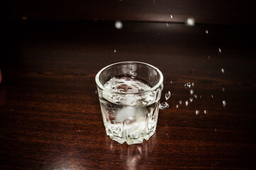 Splashing water from a transparent glass on a red wooden background