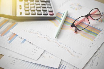 Naklejka na ściany i meble Financial graphs and charts with eyeglasses, calculator on desk.