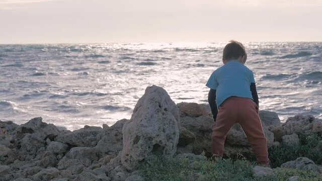 little boy dysfunctional family spends time seashore. orphan child old shabby clothing, playing alone rock throw beach windy weather. concepts loneliness and social injustice.