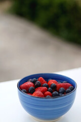 Bowl of strawberries and blueberries on a table in a garden. Selective focus.