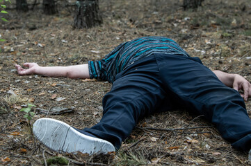 Murder in the woods. The body of a man in a blue t-shirt and trousers lies on the ground among the trees in the forest. Victim of an attack.