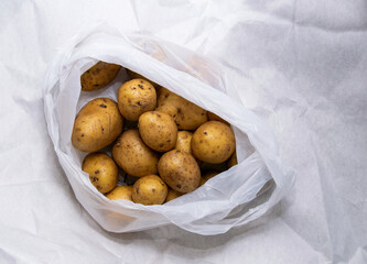 A pile of unwashed potatoes lies in a white bag
