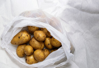 A pile of unwashed potatoes lies in a white bag