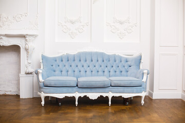 Blue soft sofa in light interior with fabric upholstery. Elegant royal luxury interior with white walls and blue sofa