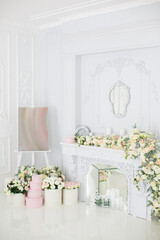 Elegant white fireplace full of flowers. Elegant white room decorated with easel and hat boxes. Wedding decorated area. Vintage decor in light interior