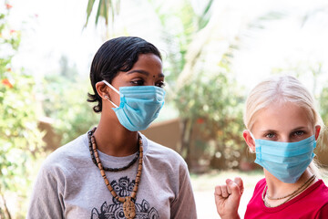 portrait of two Caucasian and African girls in protective medical masks, coronavirus concept....