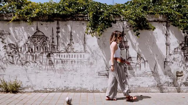 Woman with fanny pack and sunglasses walking on a wall with Istanbul paintings , Turkey