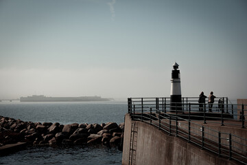 Two older women looks out over the ocean next to a lighthouse on a dream like morning by the ocean in Malmö, Sweden