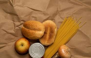 apple, spaghetti, onions, bread and canned goods lie on a paper bag