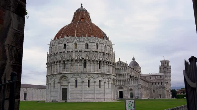 Wide tracking shot of the Leaning Tower of Pisa, Cathedral and baptistery in Piazza dei Miracoli, Italy, featuring the famous bell tower. Square deserted due to the coronavirus pandemic