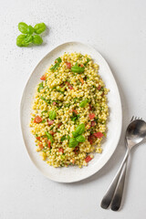 Homemade pasta ptitim with vegetables decorated basil leaves on white background. Top view. Vertical format.