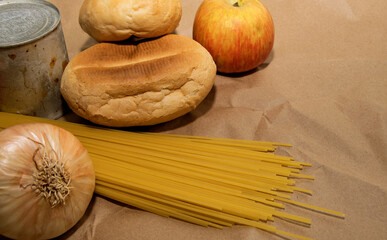 apple, spaghetti, onions, bread and canned goods lie on a paper bag