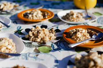 Dining table on the ground with many plates of oatmeal, banana. Summer breakfast outside

