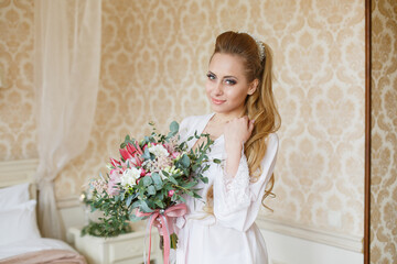 Pretty young Bride. Blonde-haired woman with wedding hair-style with a long tail. Boudoir morning of the bride. Looking on her bouquet