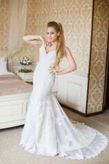 Fototapeta premium Pretty young Bride. Blonde-haired woman with wedding hair-style with a long tail. Boudoir morning of the bride. Looking to the camera