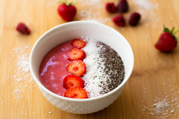 Healthy vegan trendy breakfast: magenta pink berry smoothie bowl made with frozen bananas, raspberry, strawberry and coconut milk. Topped with coconut flakes chia seeds and sliced strawberry. 