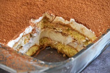 Close up a tiramisu cake in glass baking tray, homemade gluten-free Italian layered dessert with ladyfinger biscuit and mascarpone cream decorated with cocoa powder