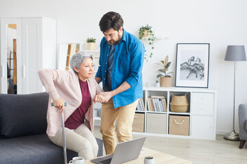 Fototapeta premium Man helping senior woman to stand up he support her while they are in the living room at home
