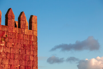 Pointed merlons and crenels at the top of a medieval castle. Fortification wall built of stone blocks. Watch tower of Fernandine walls in Porto Portugal against clear blue sky with some clouds.